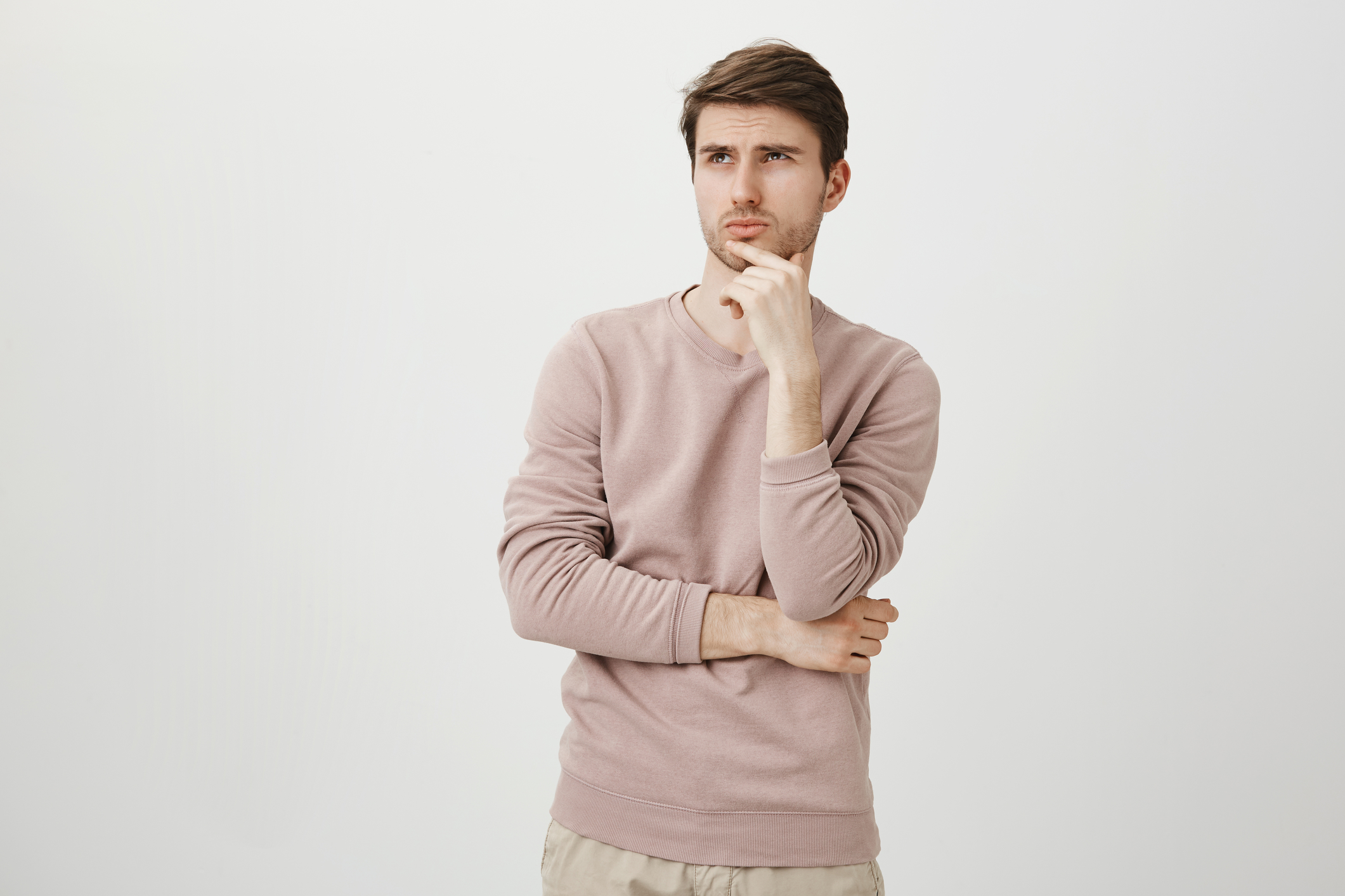 Portrait of attractive young man with bristle looking up while touching chin and thinking about something