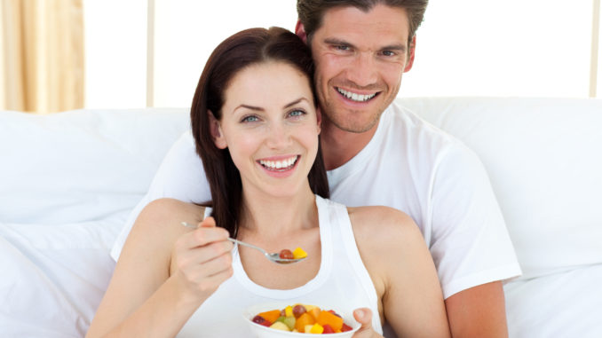Happy couple eating fruits lying on their bed at home