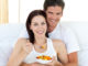 Happy couple eating fruits lying on their bed at home