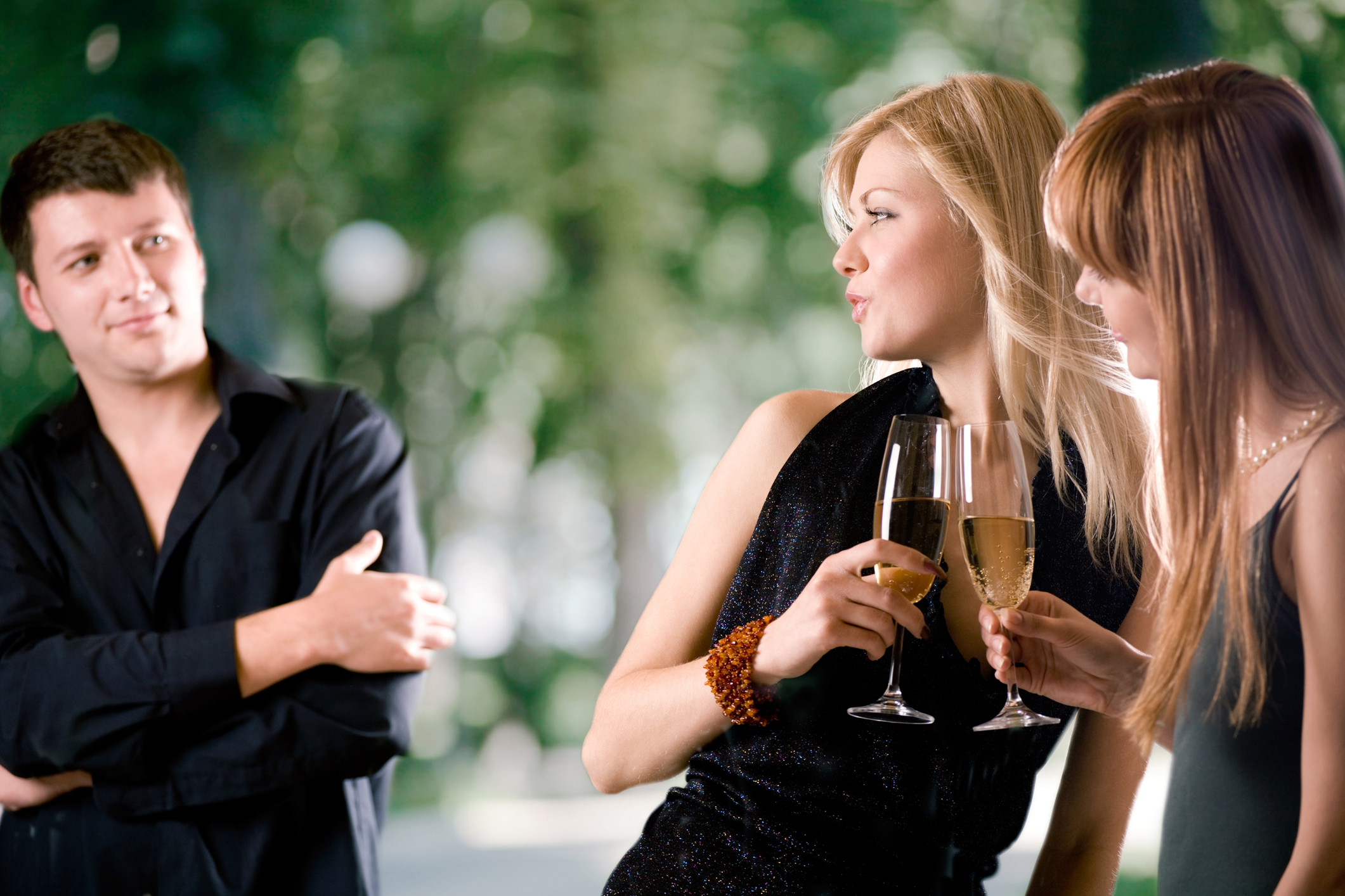 Two women holding glasses with champagne and laughing, young man looking at them