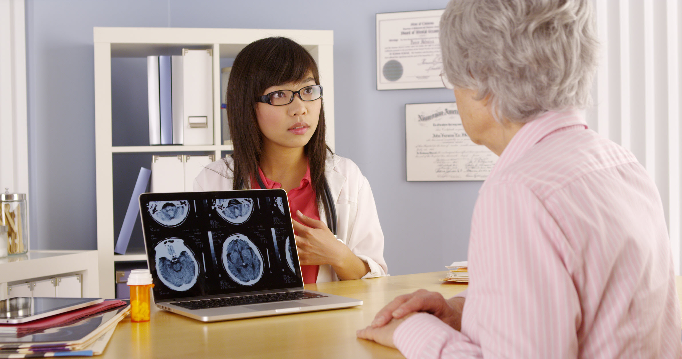 Asian doctor explaining brain scans to elderly patient.