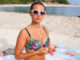 Girl sitting on the beach near see and using phone.