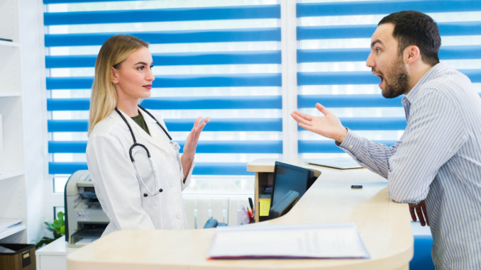 Man talking to female receptionist at hospital.