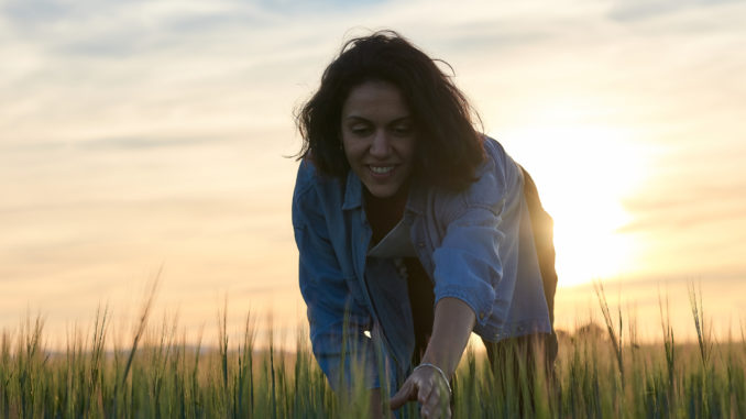 She is smiling and picking some herbs from the field.