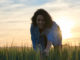 She is smiling and picking some herbs from the field.