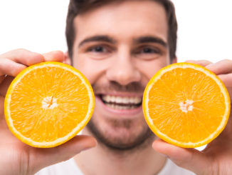 Young man is holding oranges in front of his eyes. Close-up.