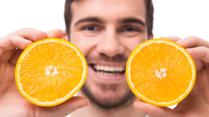 Young man is holding oranges in front of his eyes. Close-up.