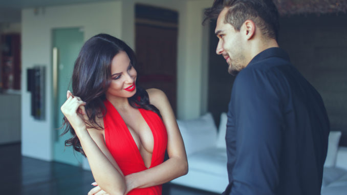 Woman in red dress and lis flirting with young men indoors, playing with hair