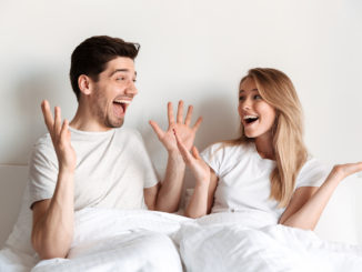Image of young happy excited loving couple lies in bed looking at each other with mouth opened.