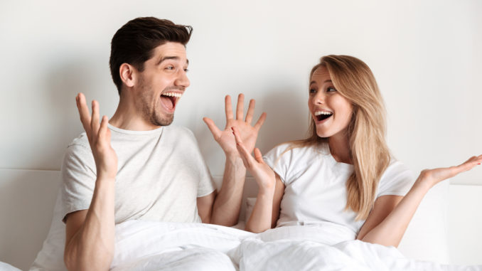 Image of young happy excited loving couple lies in bed looking at each other with mouth opened.