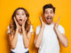 Photo of excited couple men and women in basic clothing shouting in surprise or delight and raising arms isolated over yellow background