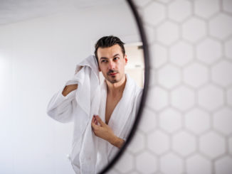 Young man in the bathroom in the morning routine, reflection in mirror.