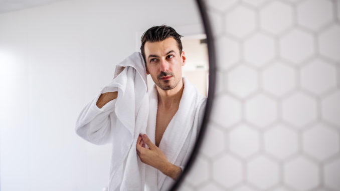 Young man in the bathroom in the morning routine, reflection in mirror.