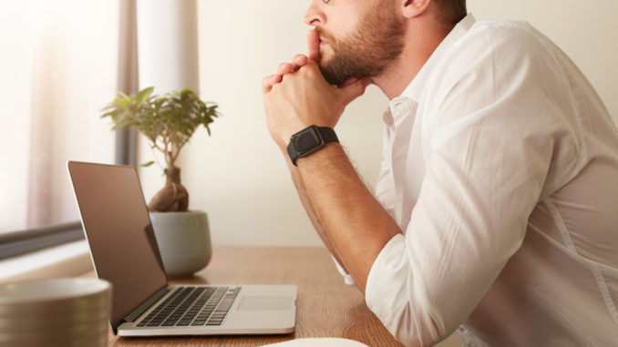 Side view of businessman sitting at his desk with a laptop and looking away. Man at his workdesk thinking of business