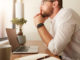 Side view of businessman sitting at his desk with a laptop and looking away. Man at his workdesk thinking of business