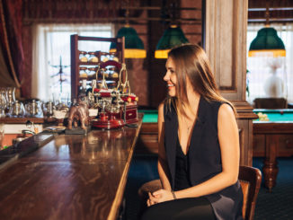 Beautiful young woman sitting at the bar talking with the bartender,the girl smiles in the bar