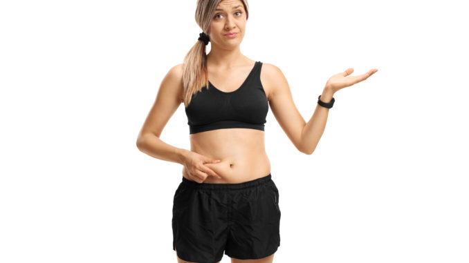 Young woman touching her belly fat and gesturing with her hand isolated on white background