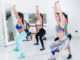 Young slender women doing overhead squat exercise during group training in gym.