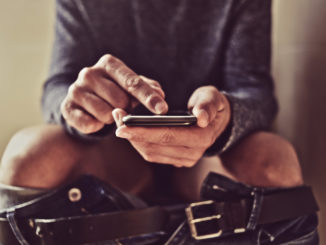 Closeup of a young caucasian man using his smartphone in the toilet while sitting in the bowl