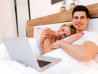 Happy couple in bed using notebook and smiling