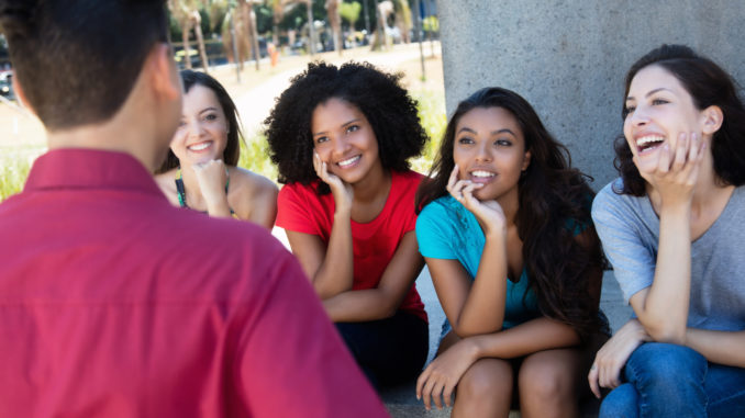 Group of multi ethnic girls flirting with one guy outdoors in summer