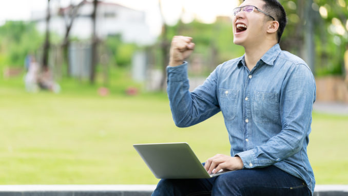 Attractive asian happy man gesture or raise hand excited screaming yes reading online