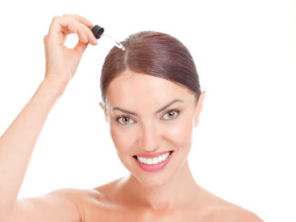 Woman applying serum essence essential oils to her hairline for growth