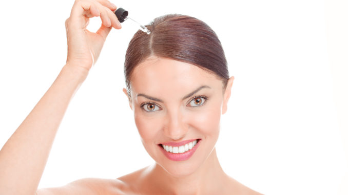 Woman applying serum essence essential oils to her hairline for growth