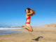 Carefree healthy bikini woman jumping on the beach.