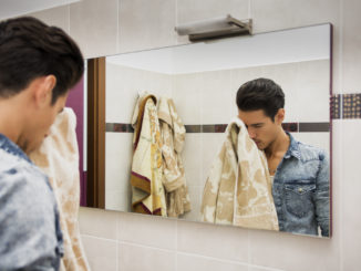 Reflection of Young Man Drying Face with Towel in Mirror as Part of Daily Hygiene Routine