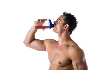 Muscular shirtless male bodybuilder drinking protein shake from blender. Isolated on white, looking to a side, profile view.