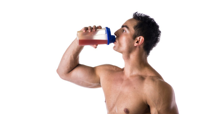 Muscular shirtless male bodybuilder drinking protein shake from blender. Isolated on white, looking to a side, profile view.