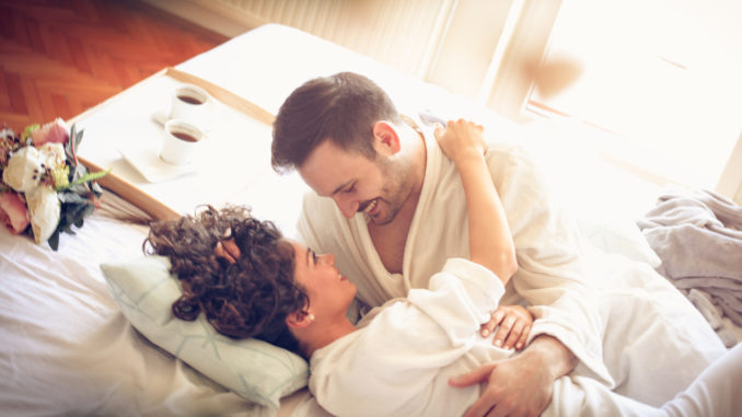 Young happy couple lying together in bed. Couple looking each other.