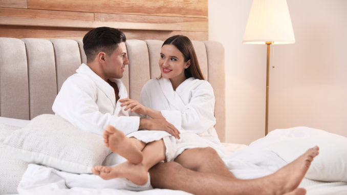 Happy couple in bathrobes resting on bed at home