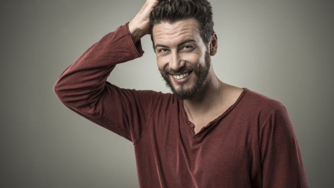 Doubtful smiling young man touching his head and thinking