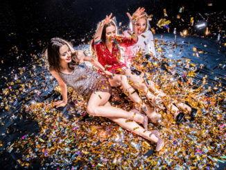 Three stylish young women sitting on the floor covered with confetti