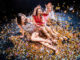 Three stylish young women sitting on the floor covered with confetti