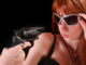 Young redhead woman and gun to her face on black background