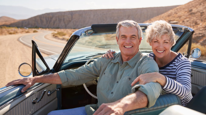 Senior couple smile to camera from open top car, close up