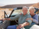 Senior couple smile to camera from open top car, close up