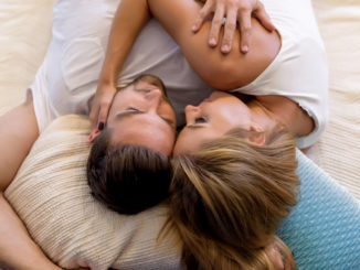 A beautiful young couple laying on the bed and cuddling.