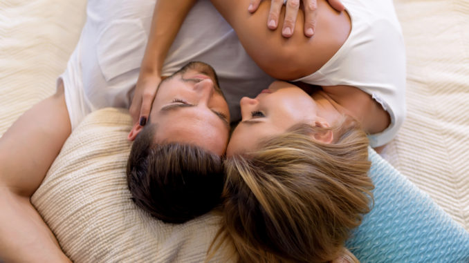 A beautiful young couple laying on the bed and cuddling.