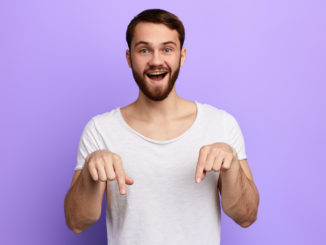 Handsome positive bearded man pointing down with two fingers.