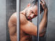 selective focus of handsome man with eyes closed taking shower in bathroom