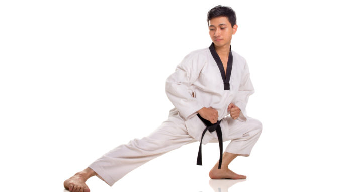 Full length portrait of a male traditional martial art practitioner stretching his right leg