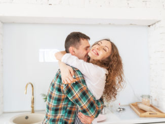 Happy beautiful young couple have fun in the kitchen, dancing, cuddling, cooking food together.