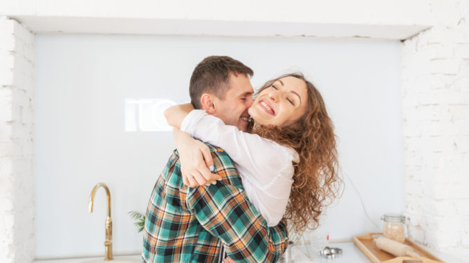 Happy beautiful young couple have fun in the kitchen, dancing, cuddling, cooking food together.