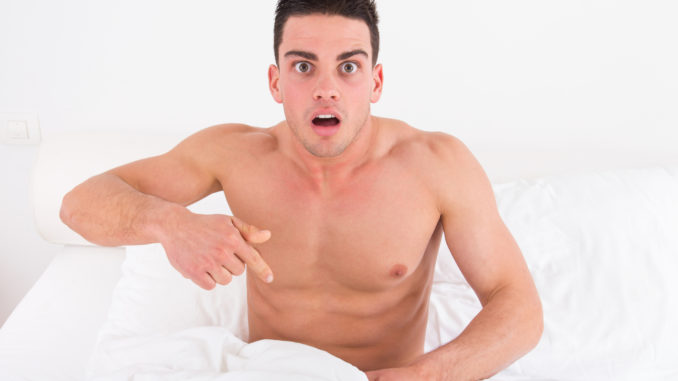 Surprised and shocked half naked young man in bed looking down at his underwear