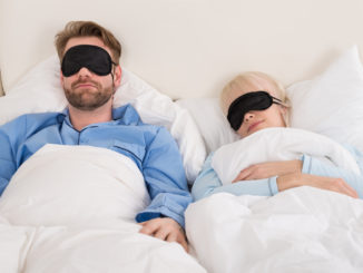 Young Couple Sleeping Comfortably On Bed Using Eye Mask
