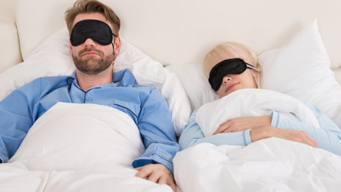 Young Couple Sleeping Comfortably On Bed Using Eye Mask